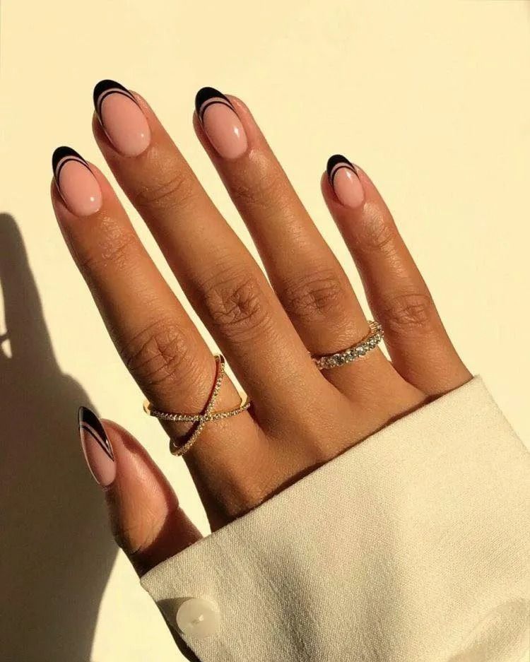Hand with oval nails, nude base with black french tip and thin black outline, two rings.