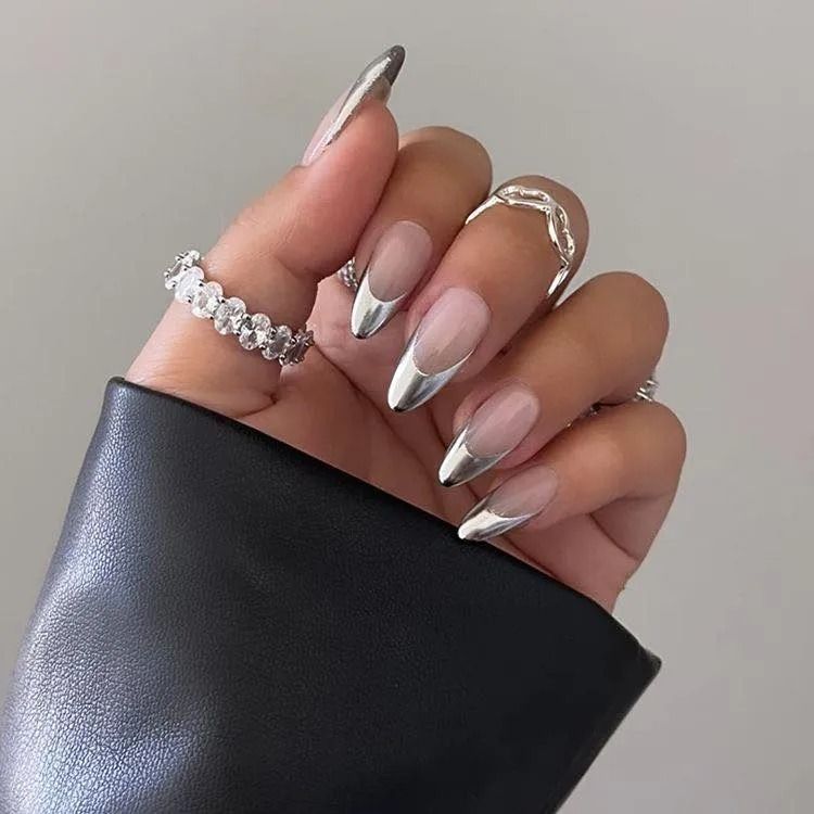 Hand with clear and metallic silver French tip nails, wearing three rings.