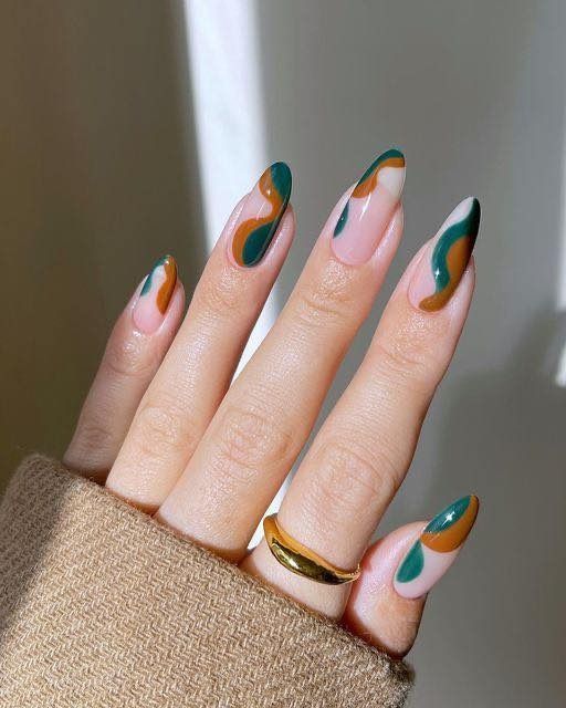 Hand with almond-shaped nails decorated with abstract green and brown swirls over a nude base, gold ring.
