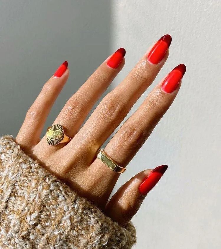 Hand with red nails, dark red tips, gold rings.