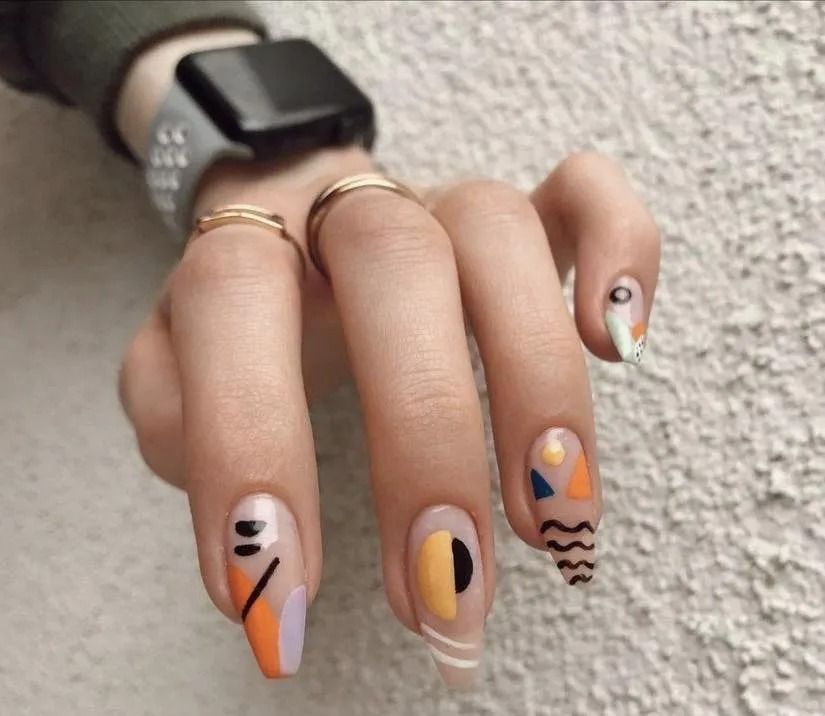 Hand with abstract art nail designs in orange, yellow, and black.