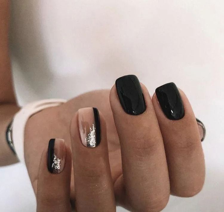 Hand with black and nude nail polish, including one with silver glitter design.