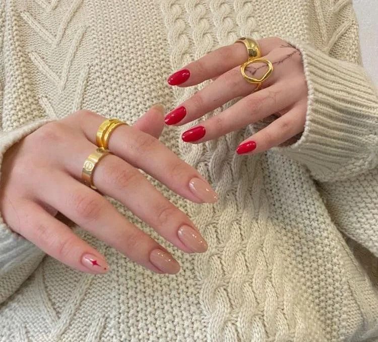 Hands with red and nude nail polish, gold rings, resting on a cream cable-knit sweater.