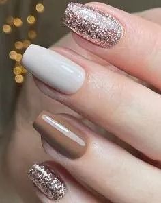 Close-up of hand with manicured nails; two with rose gold glitter, one tan, one brown.