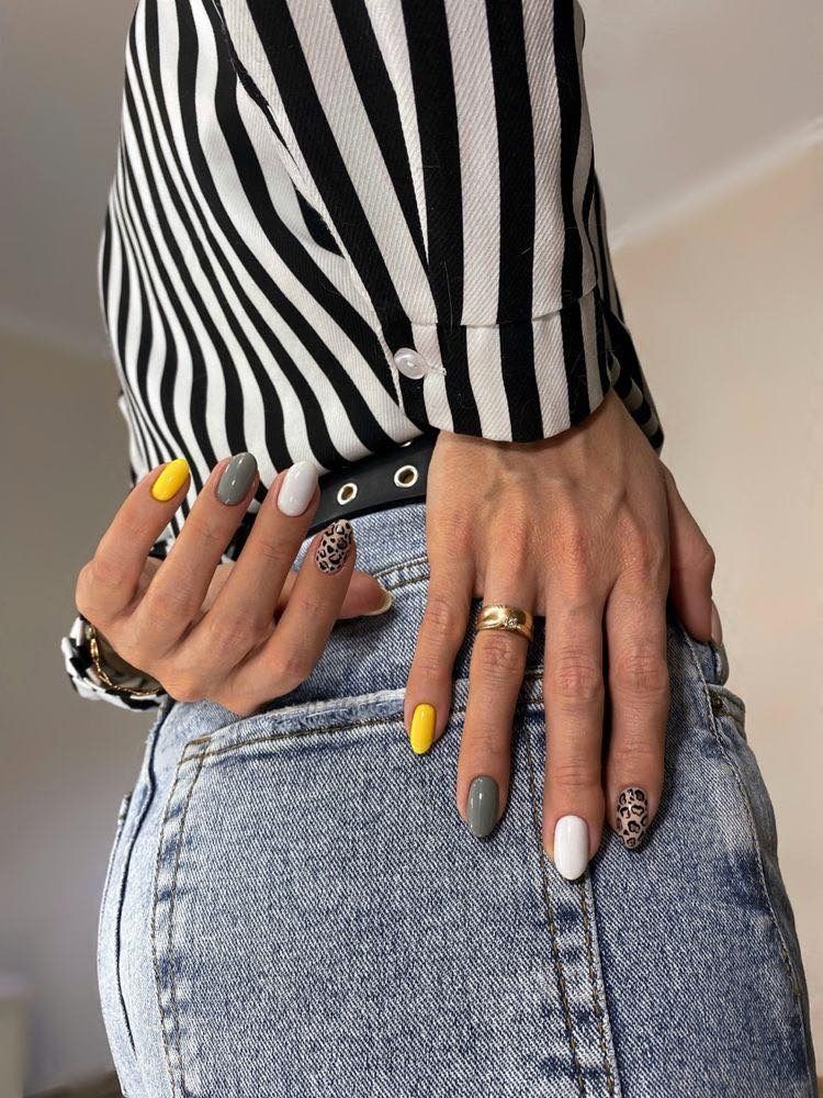 Woman's hands with painted nails in yellow, grey, and white over jeans and striped shirt.