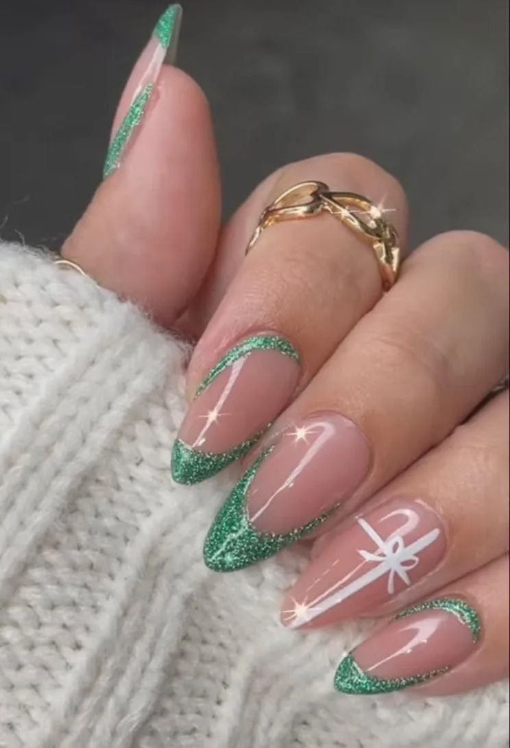 Nail art with green glitter French tips and a white bow design on an almond-shaped nail, ring on a finger.