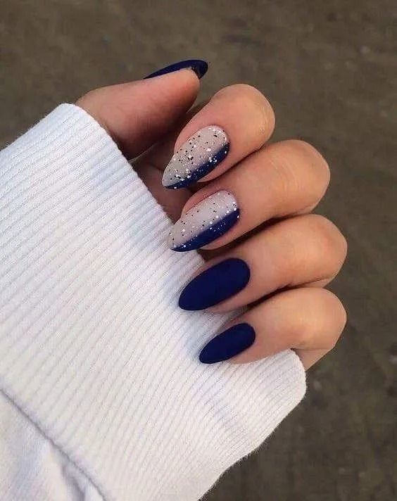 Woman's hand with almond-shaped nails. Dark blue polish on most nails, a few with sparkling silver tips.