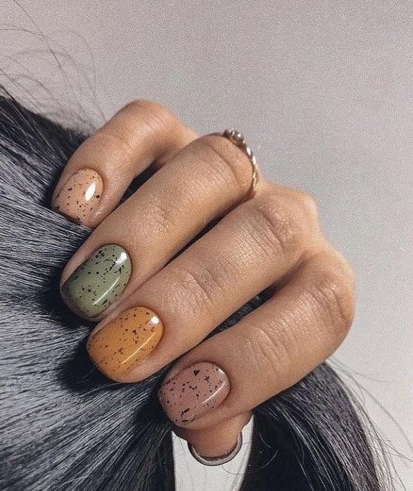 Hand with speckled, oval-shaped nails in shades of beige, green, orange, and pink, resting on hair.