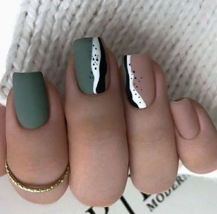 Matte nail art with green, neutral, and black designs. One finger has a gold ring.