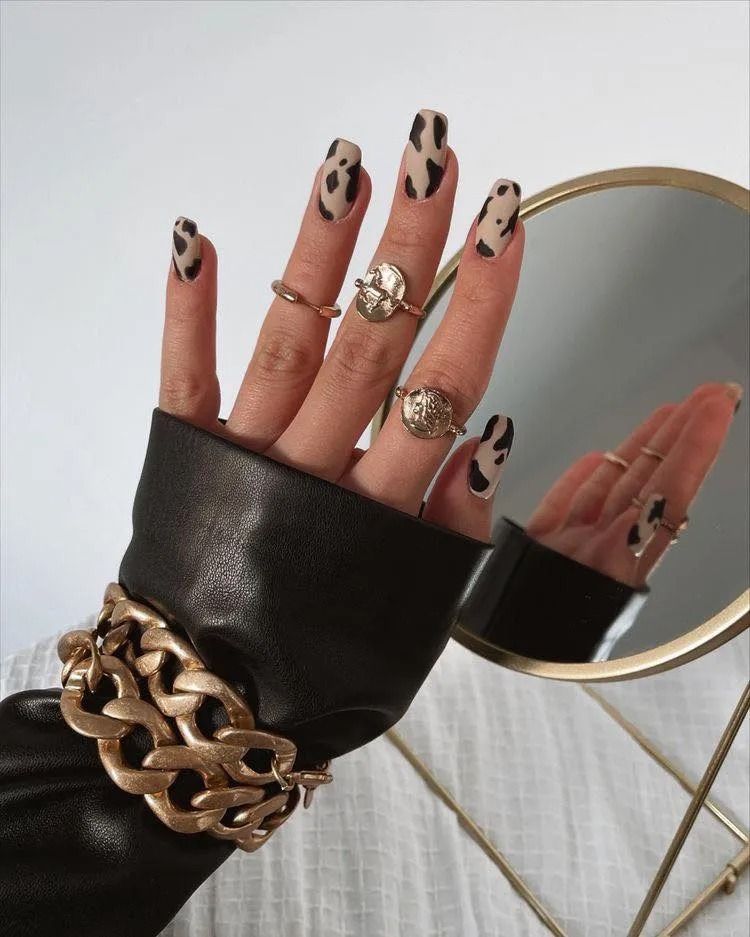 Hand with animal print nails, gold rings, and chunky bracelet, near a mirror.