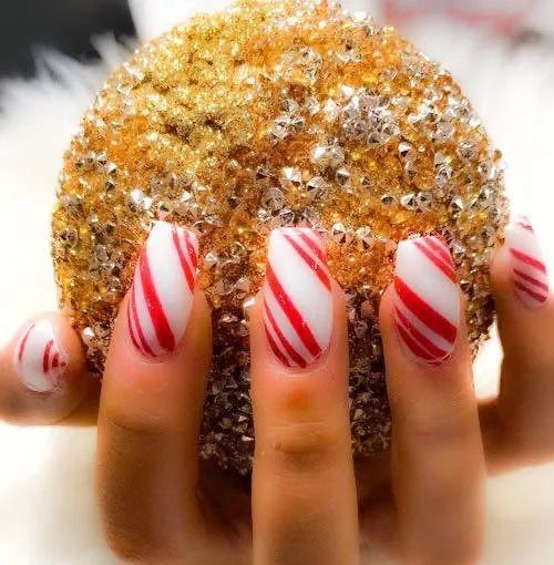 Hand holding a gold, glittery ornament with candy cane-striped nails.