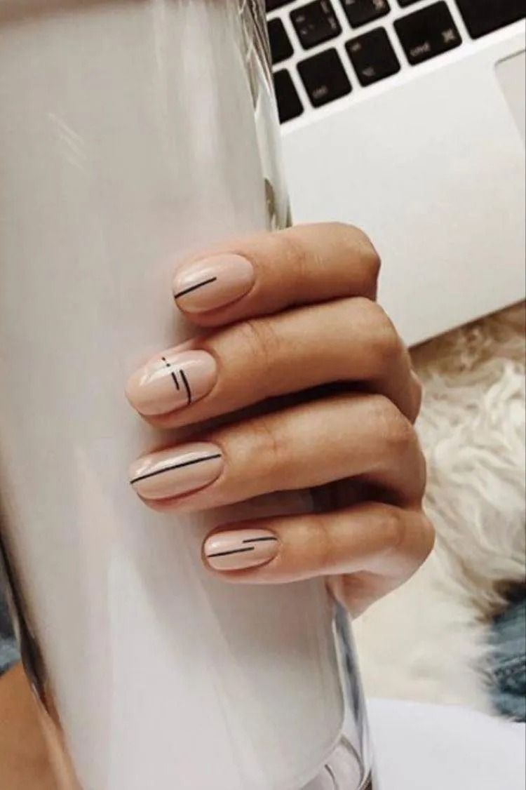 Hand with nude nails, each with a thin black stripe design, holding a white cup, laptop in the background.