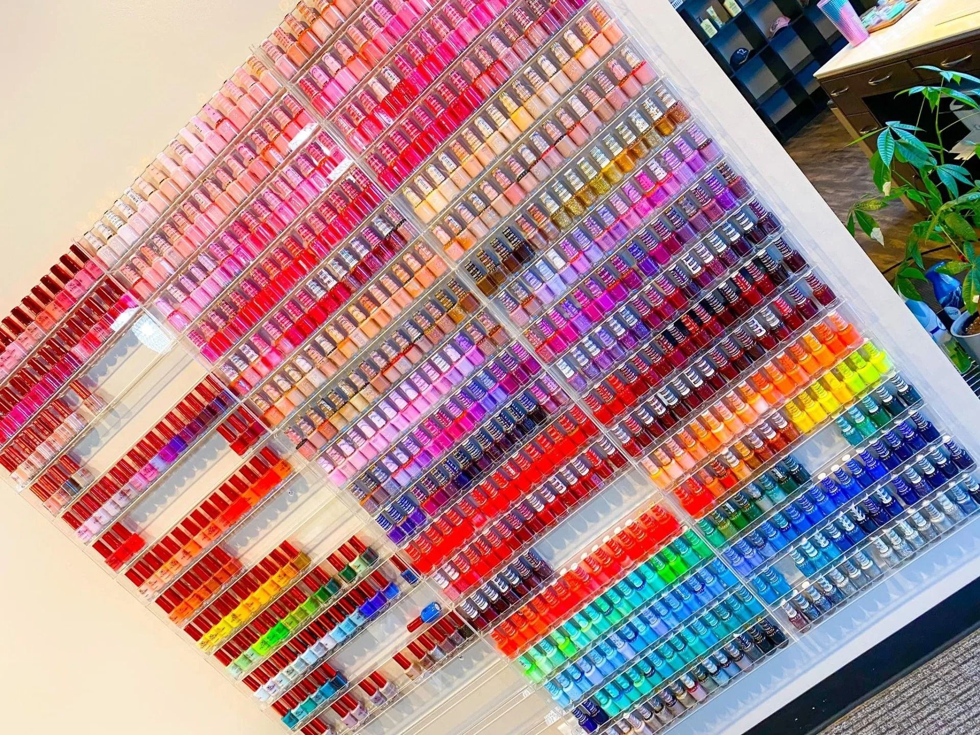 Wall display of a variety of colorful nail polish bottles arranged by color, possibly in a nail salon.
