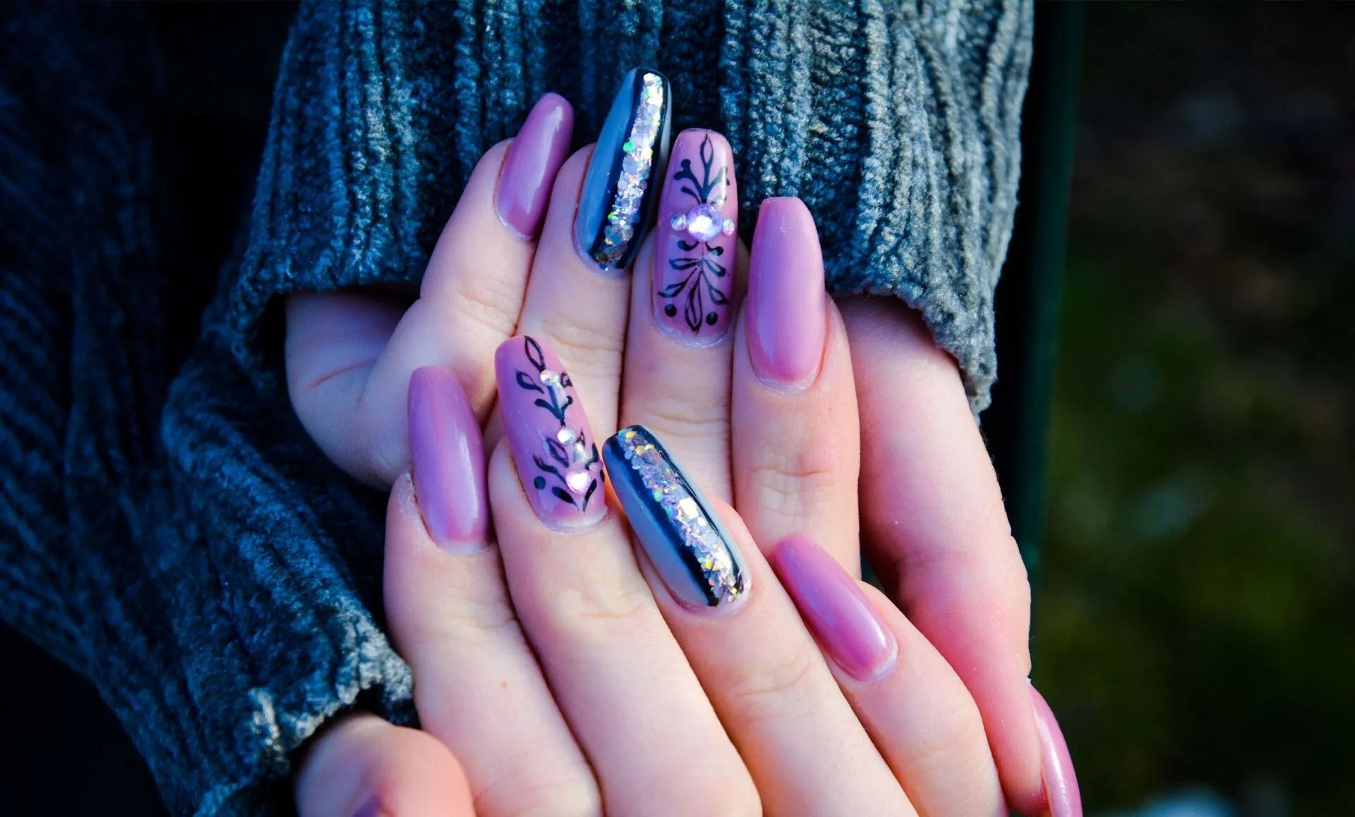 Hands with long, lavender and silver acrylic nails, some decorated with floral designs.