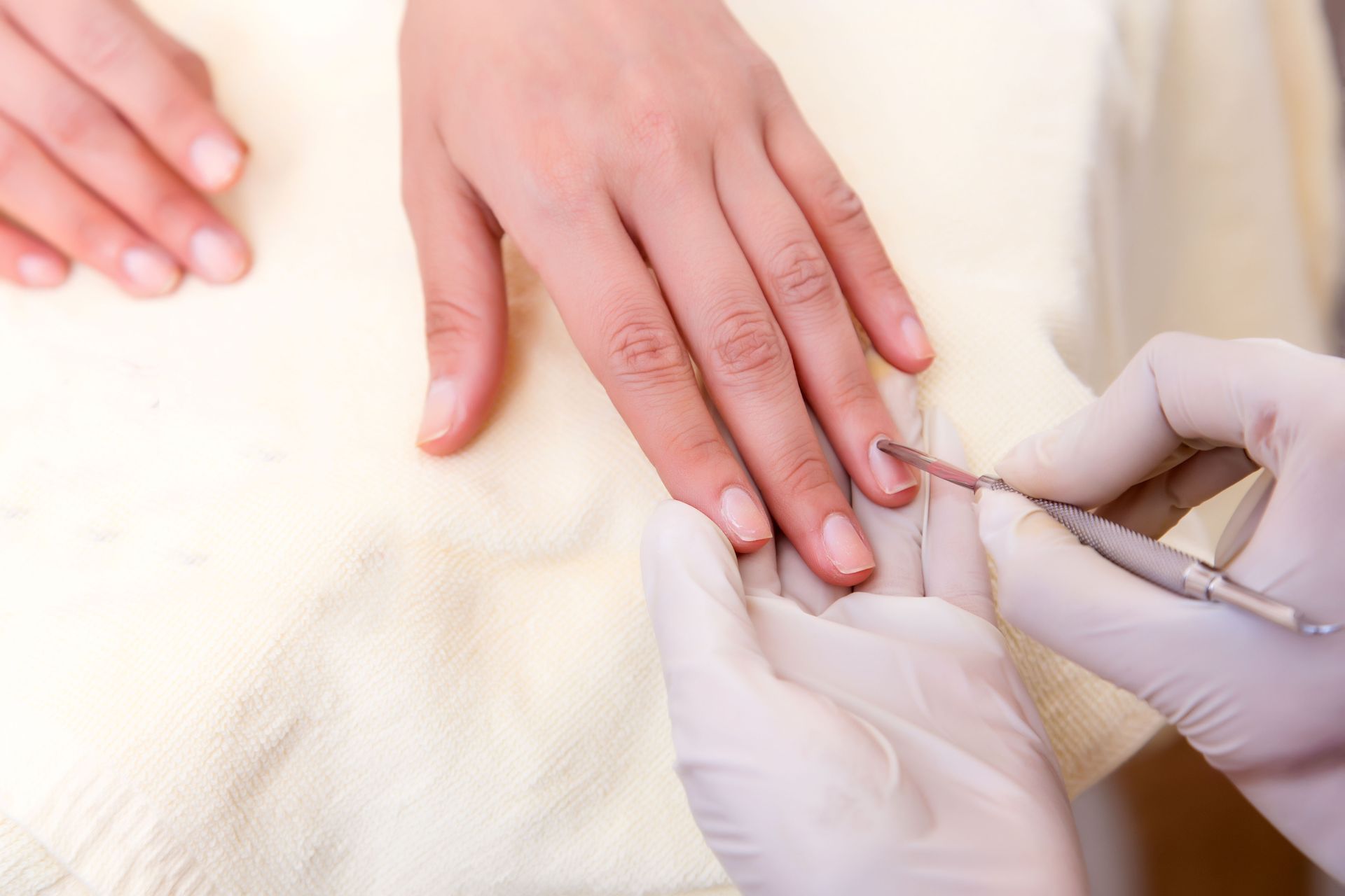 Manicurist's gloved hand using a cuticle tool on a client's fingernail.