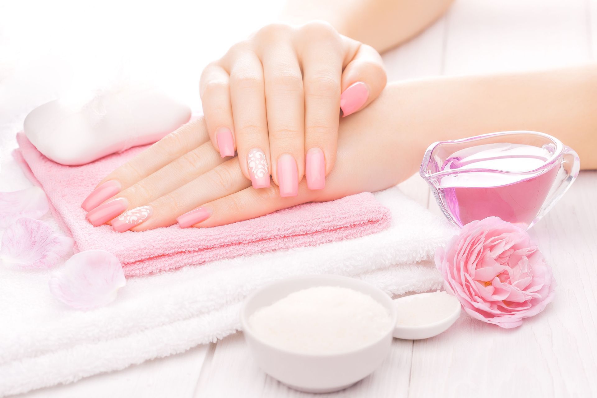 Hands with pink manicured nails, towels, and beauty products in a spa setting.