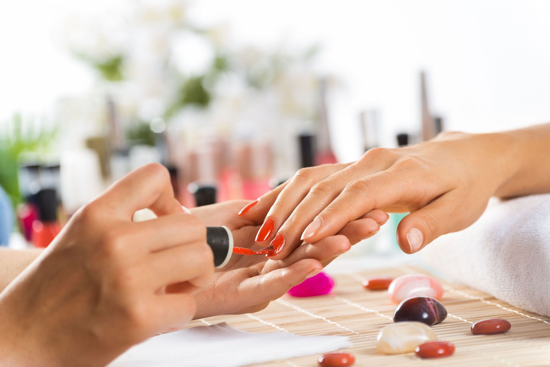 Manicurist applying red nail polish to a client's fingernails.