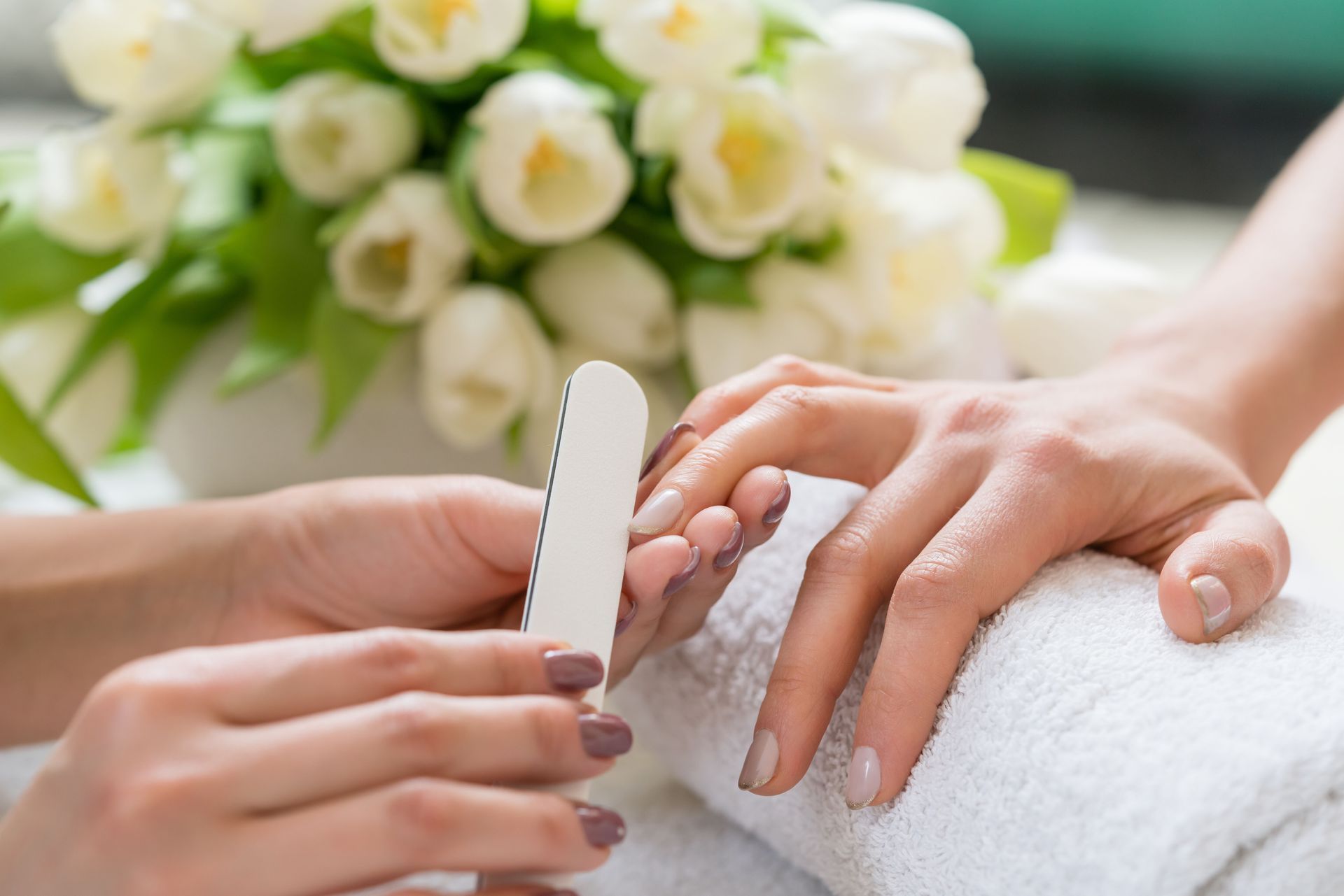 Manicure: Filing a fingernail with a nail file; white flowers in background.
