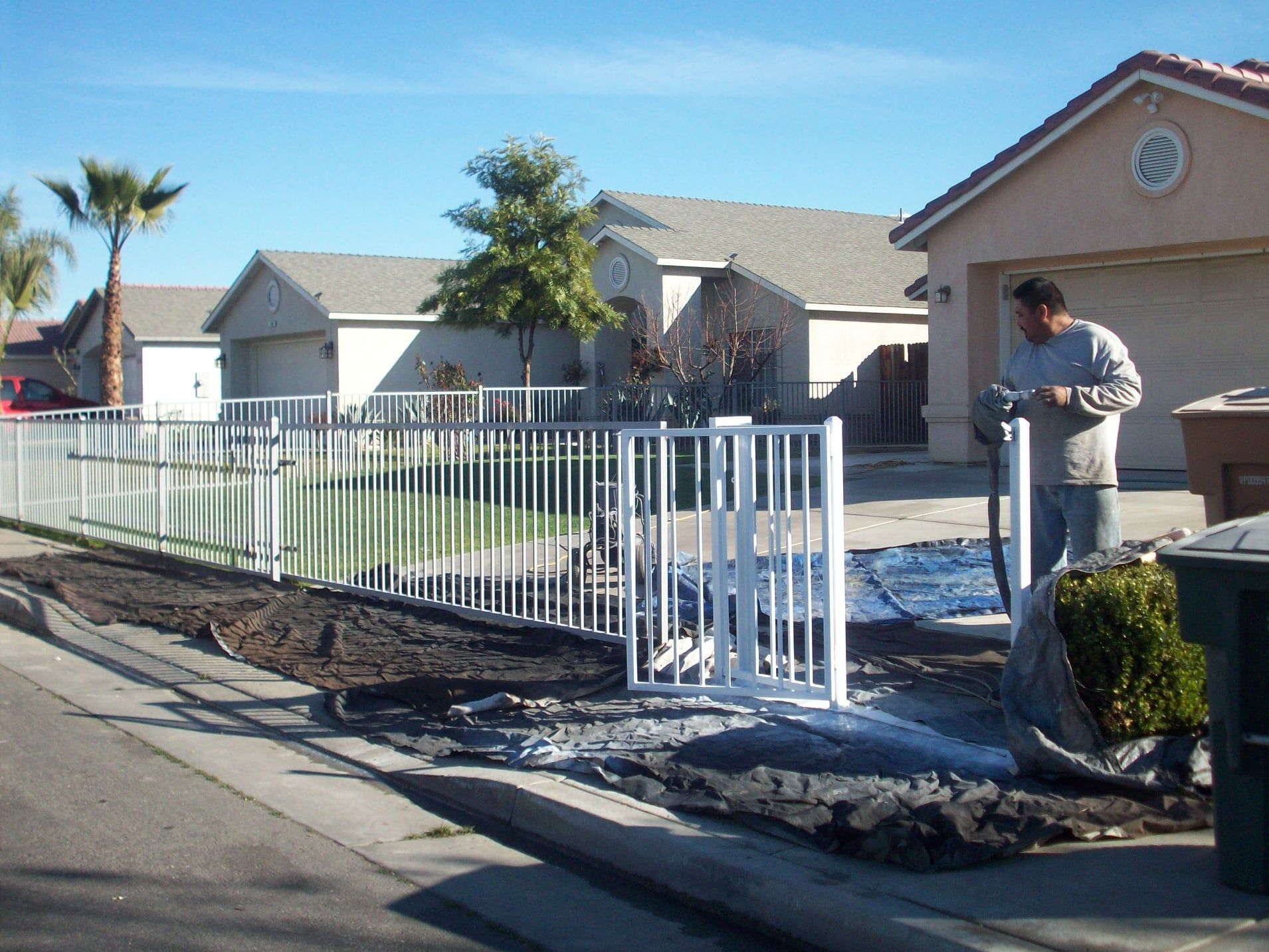 Man installing white metal fence in front yard of a house on a sunny day.