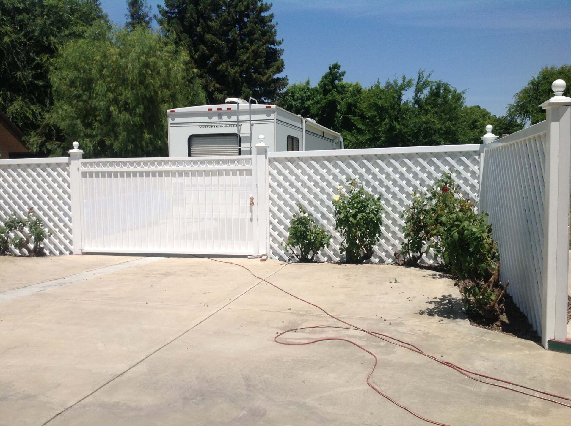 White gated fence with RV parked behind it, on a sunny day.