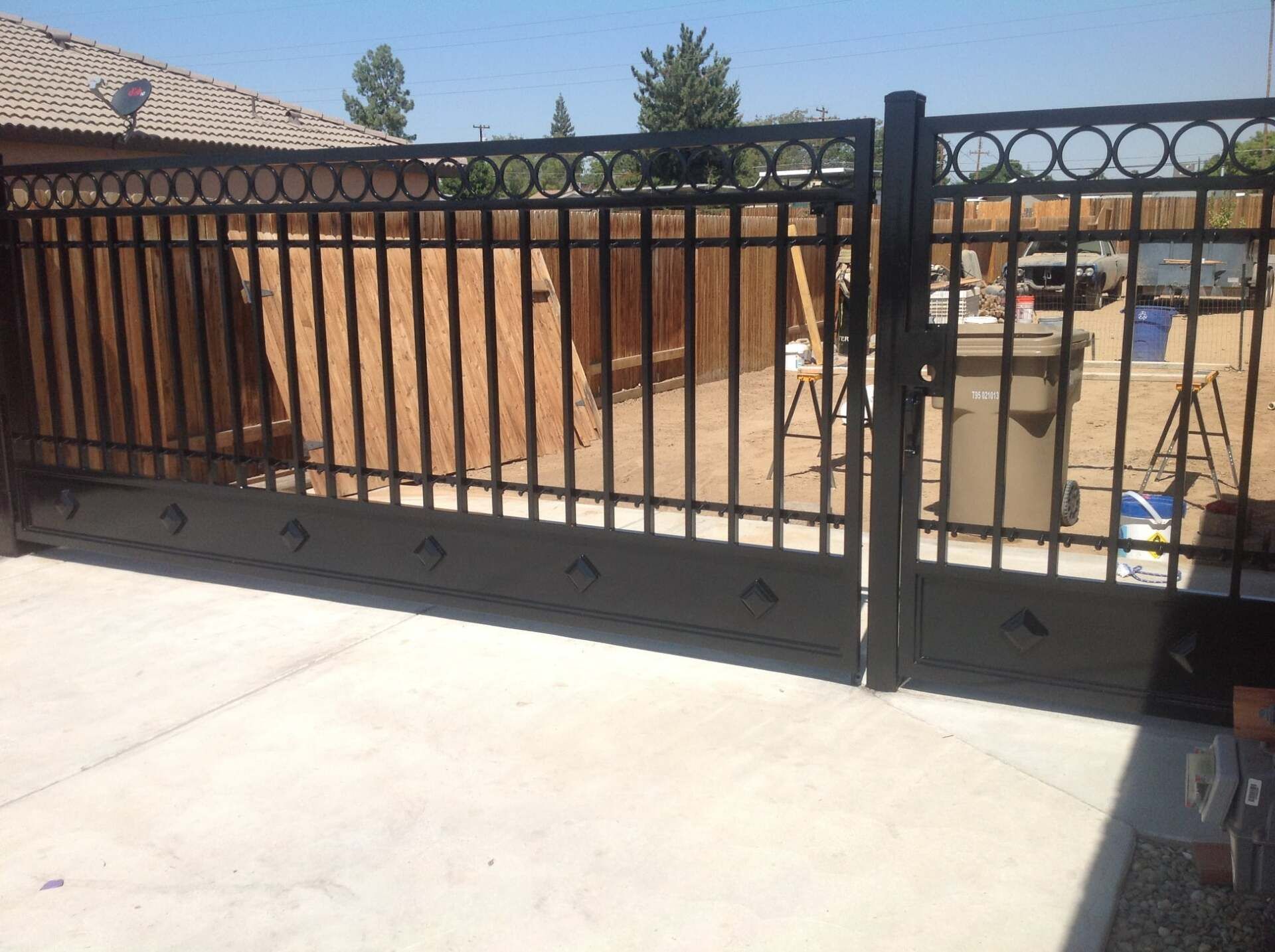 Black wrought iron driveway gate on a concrete surface, tan walls in the background, blue sky.