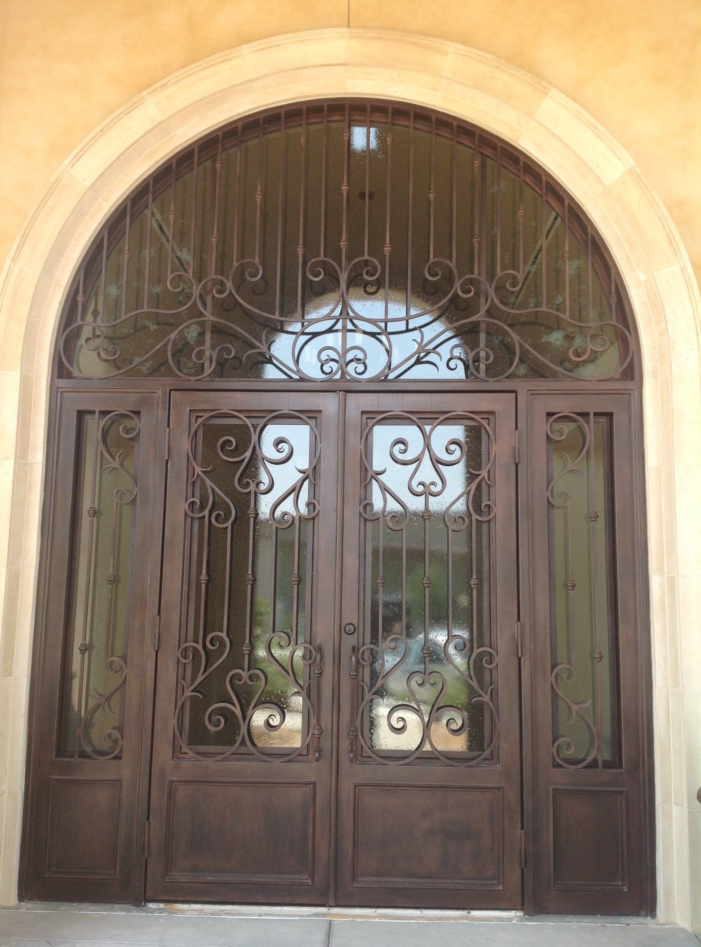 Ornate brown metal entry doors with arched transom window, set in stone facade.
