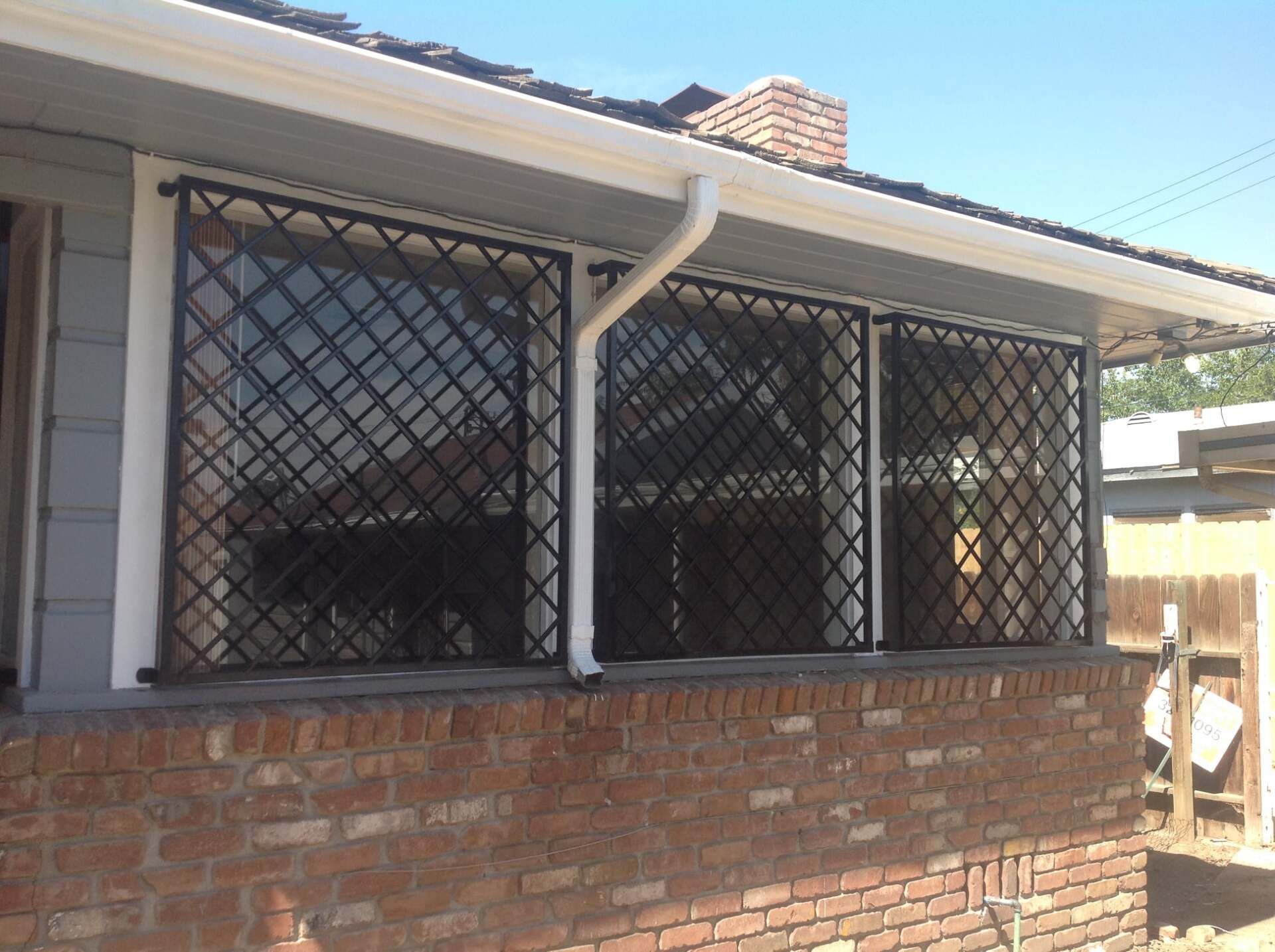 Black security grates on the windows of a brick house with white trim, under a clear blue sky.