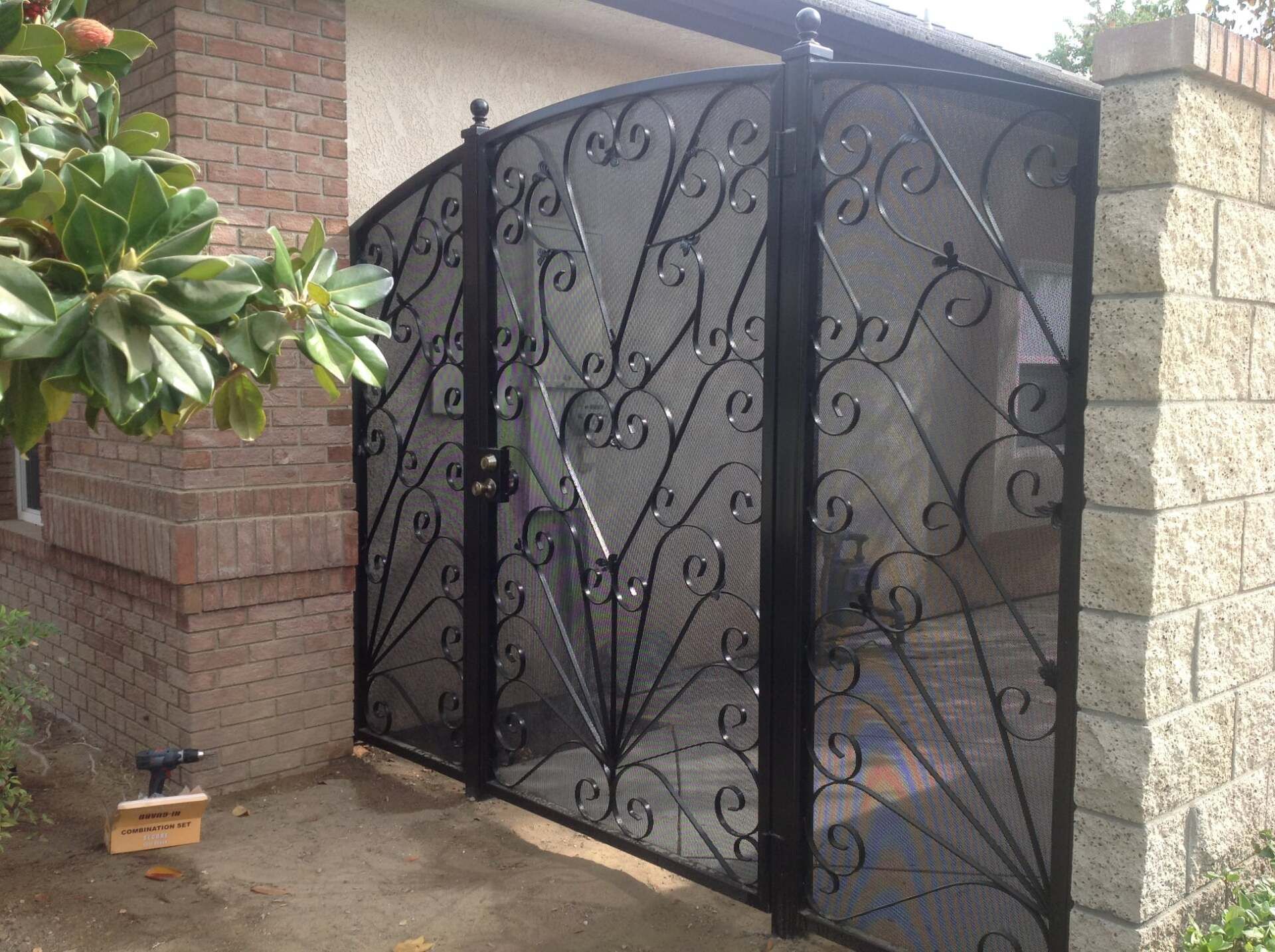 Black wrought iron gate with decorative scrollwork, set between brick and stone walls.