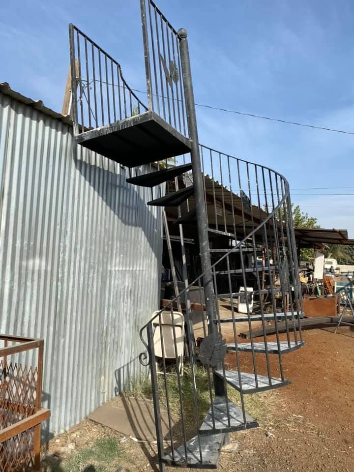 Black metal spiral staircase against a corrugated metal wall. Sunny outdoor setting.
