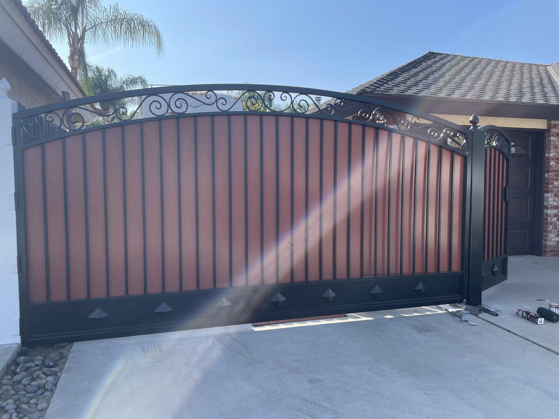 Black and brown iron gate with decorative scrollwork, set in a driveway in front of a house.