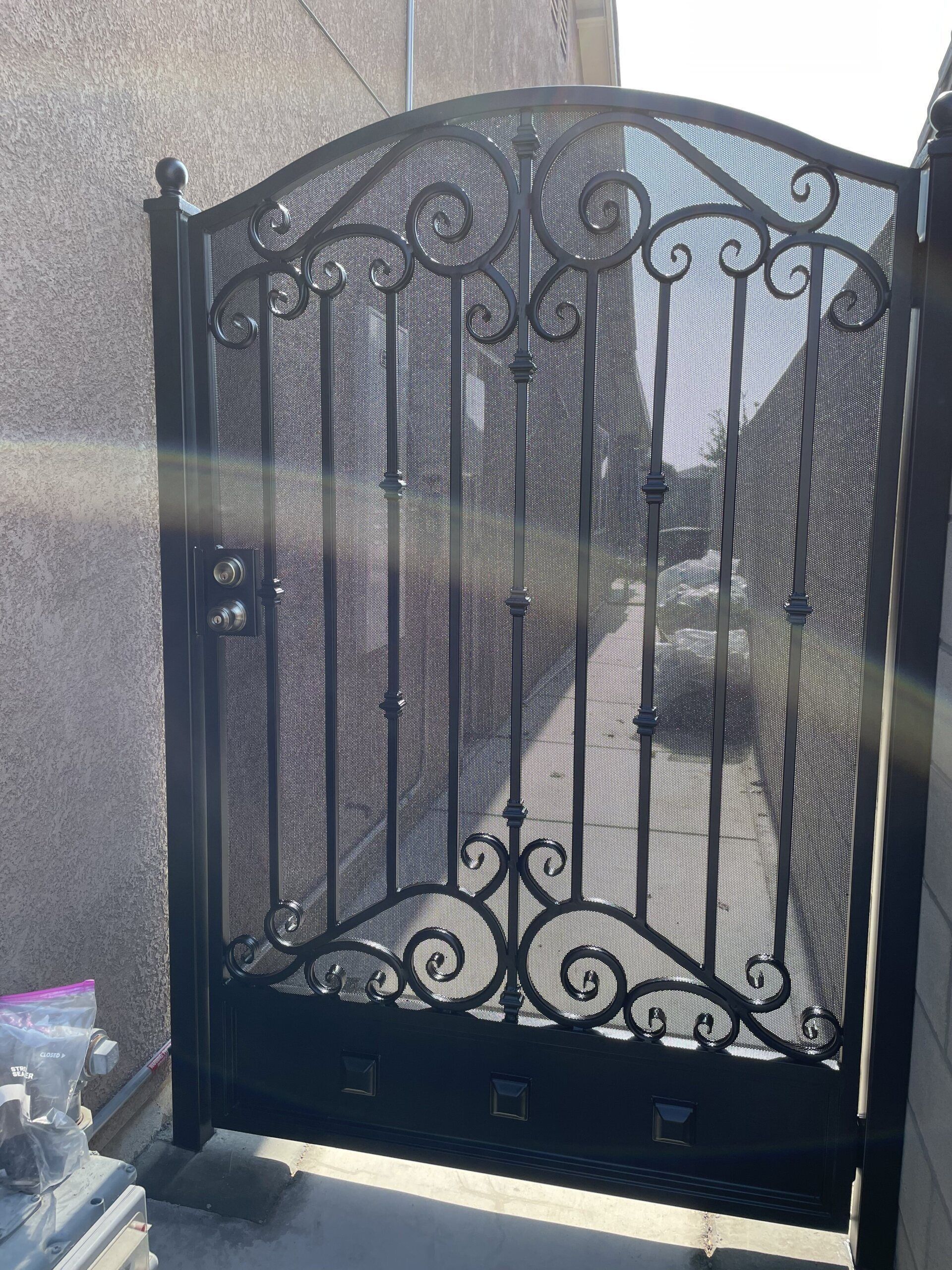 Black wrought iron gate with decorative scrollwork, mesh screen, and arched top.