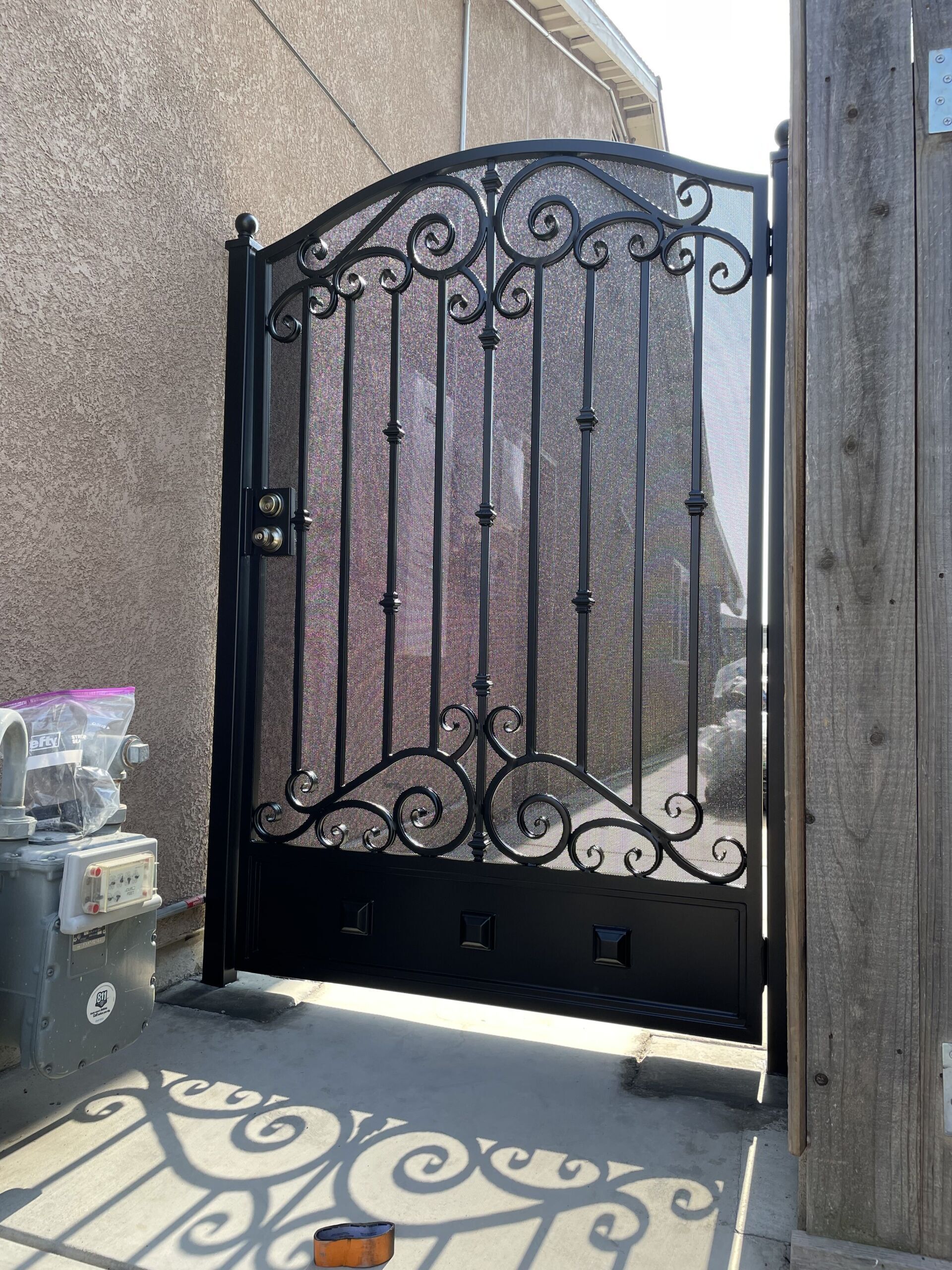 Black wrought iron gate with decorative scrollwork, mesh screen, and a lock.