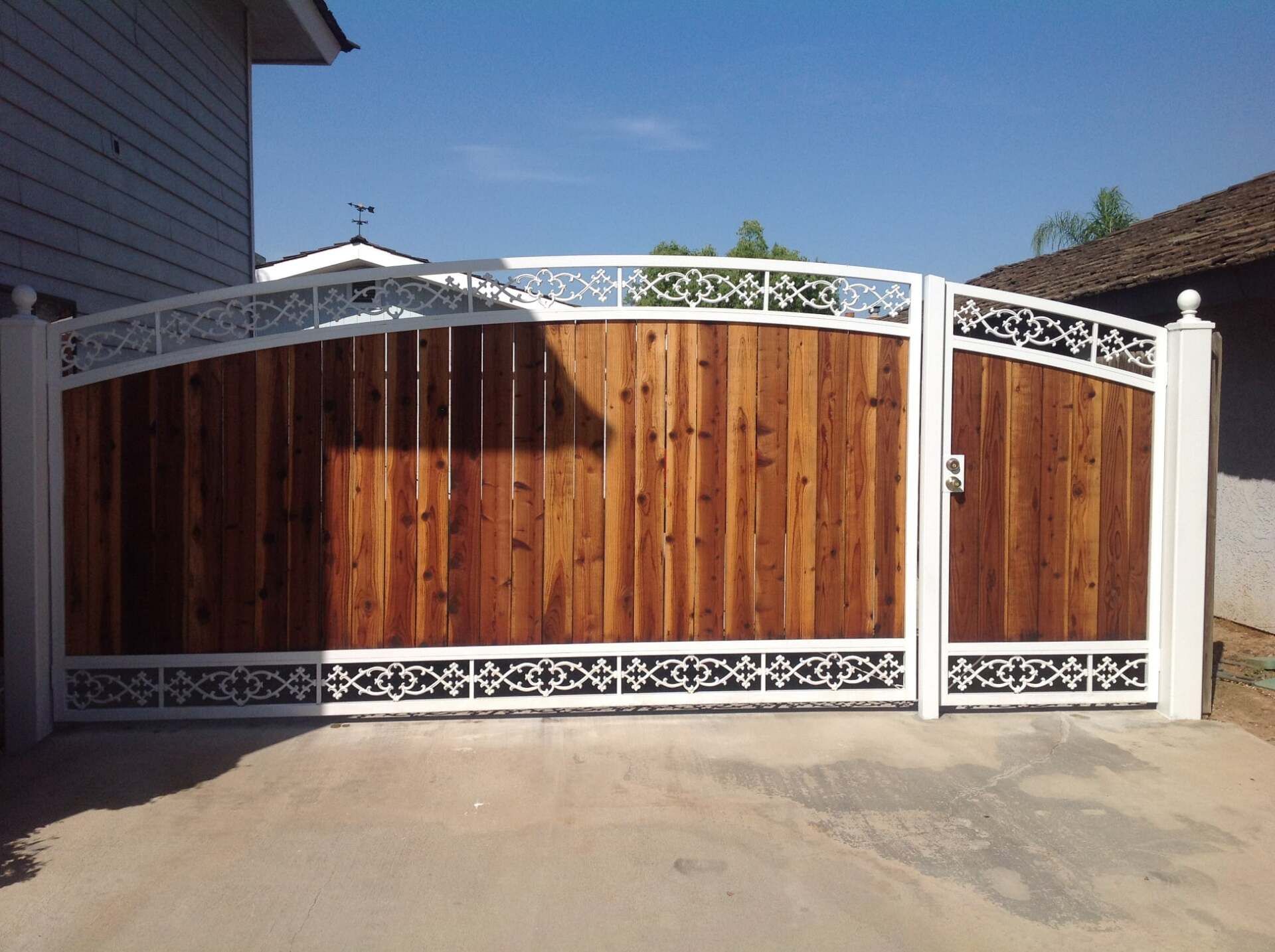 Wooden gate with white decorative metal frame, driveway, and house.