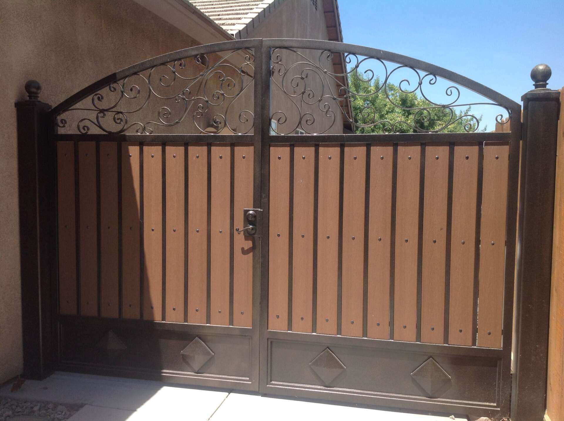 Double brown gate with vertical wood panels and decorative wrought iron top.