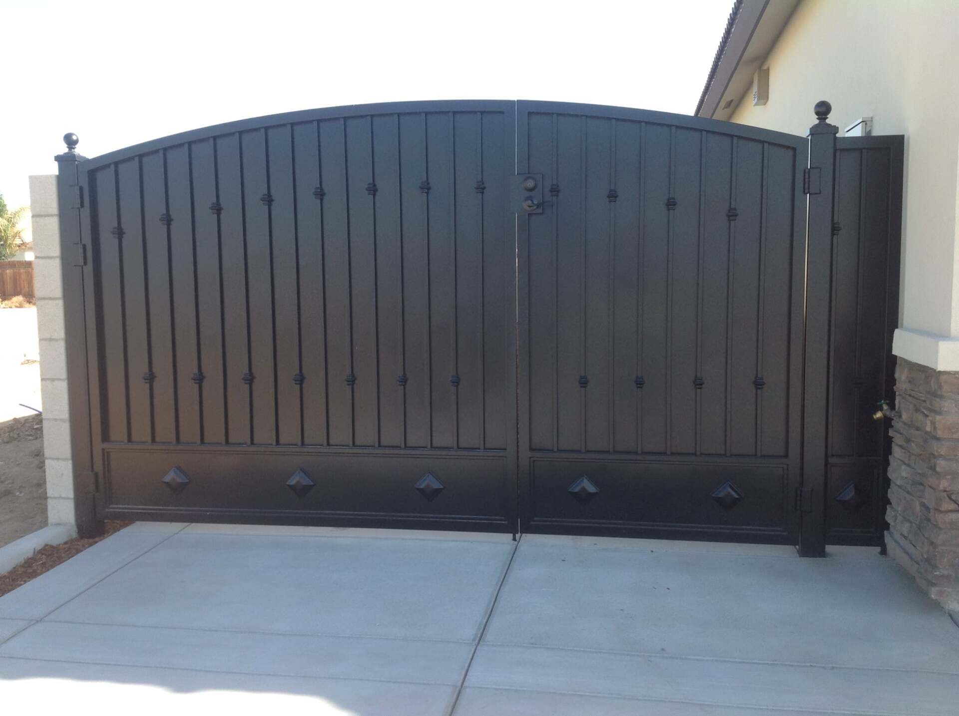 Black metal driveway gate with vertical planks and decorative hardware.