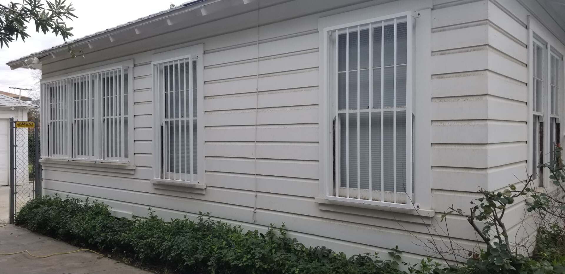 White clapboard building with barred windows. Green shrubs line the base.