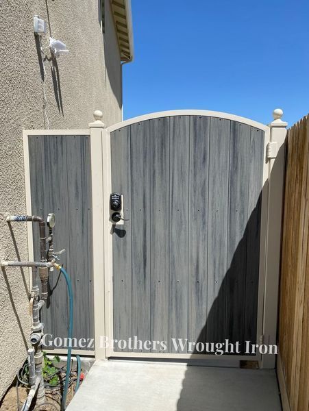 Gray and white wrought iron gate with a digital lock on a concrete walkway.