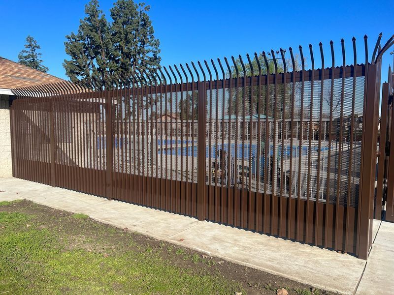Brown metal fence with vertical bars, spiked top, surrounding a yard, on a sunny day.