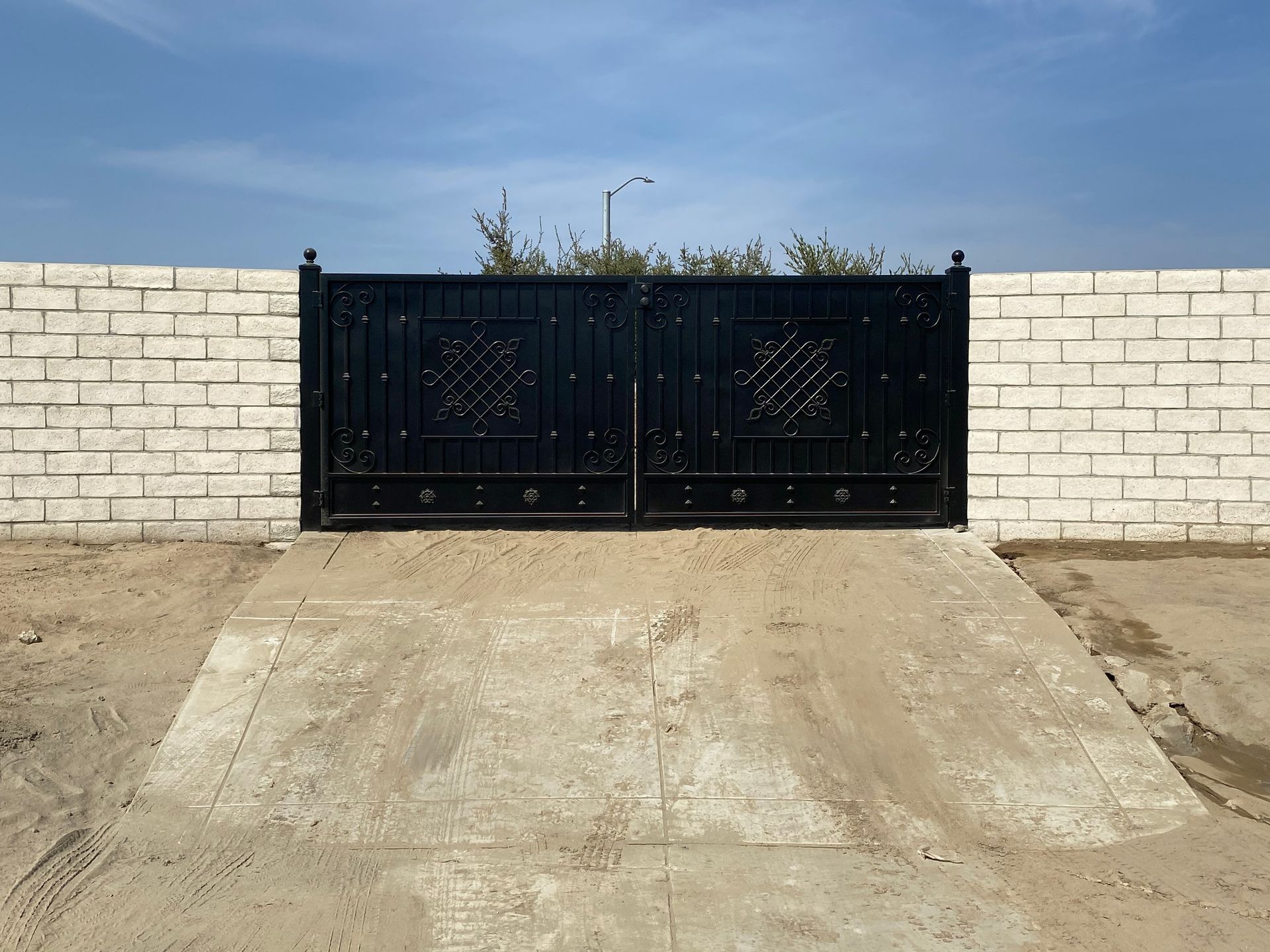 Black metal gate set into a white brick wall, over a concrete driveway.