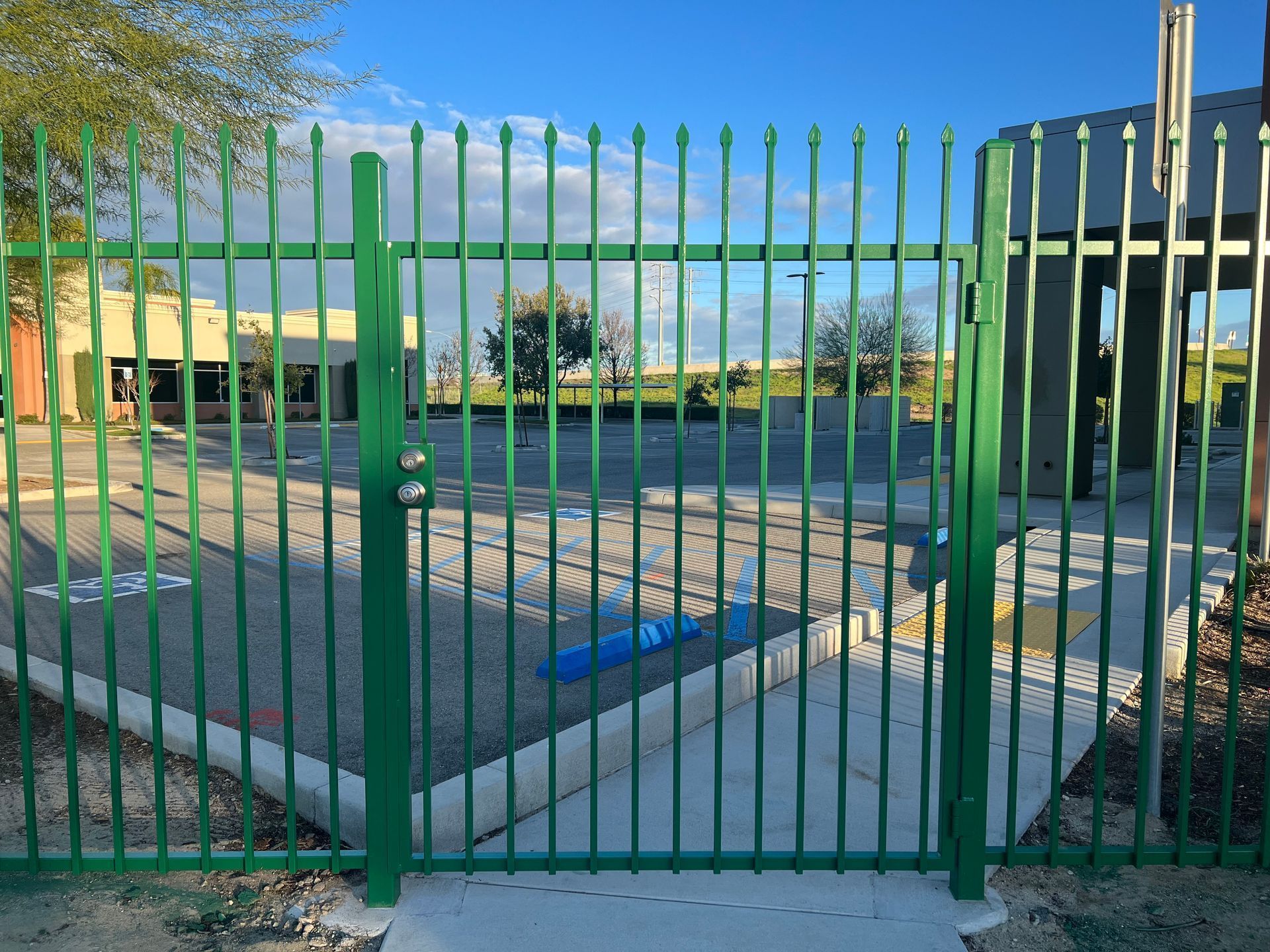 Green metal gate, locked, with a view of a building and open area beyond.