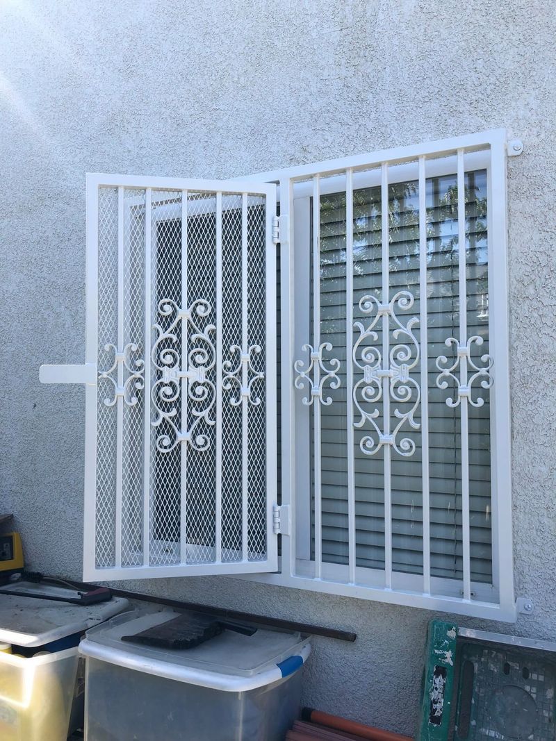 White security bars protect a window on a stucco wall. One section is open.