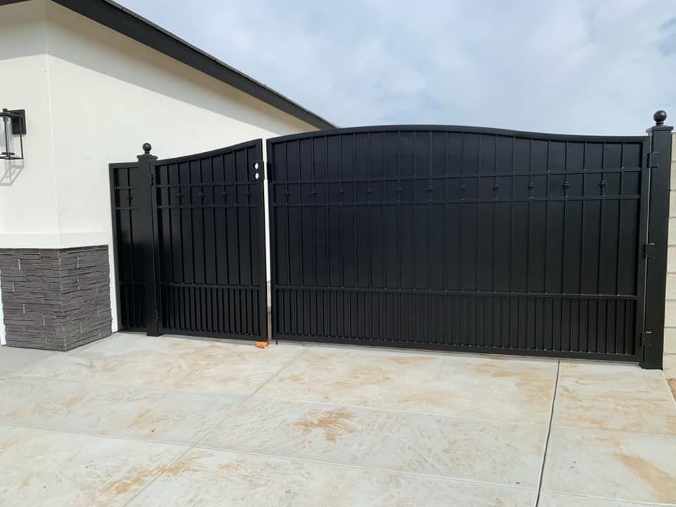 Black metal driveway gates, open, in front of a light-colored building, on concrete.
