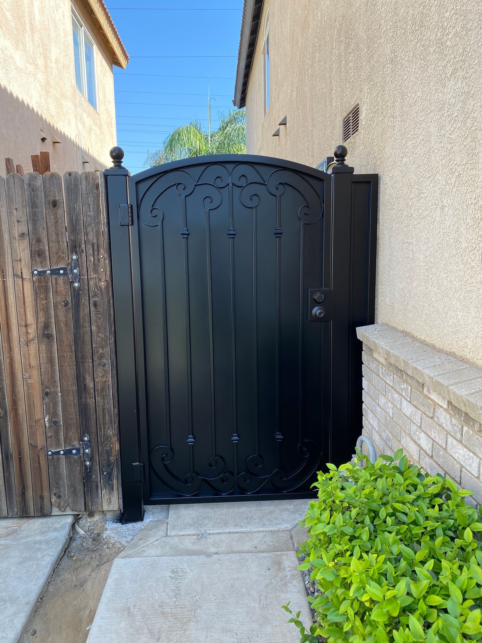 Black ornate metal gate between wooden fence and stucco wall.