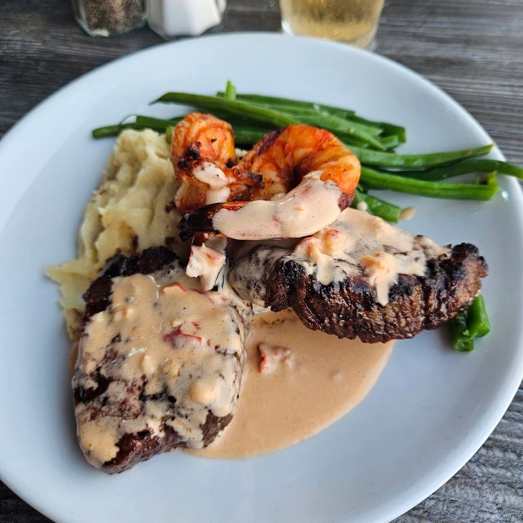 Steak and shrimp surf and turf dish on white plate with mashed potatoes and green beans.