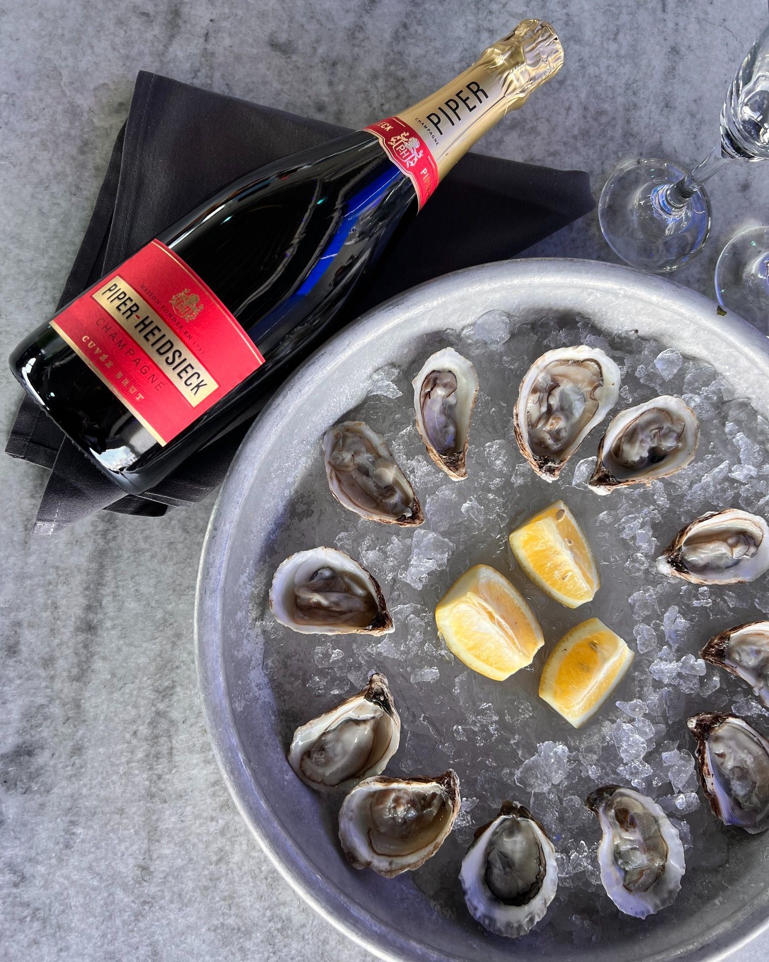 Bottle of Piper-Heidsieck champagne next to a plate of oysters on ice with lemon wedges.
