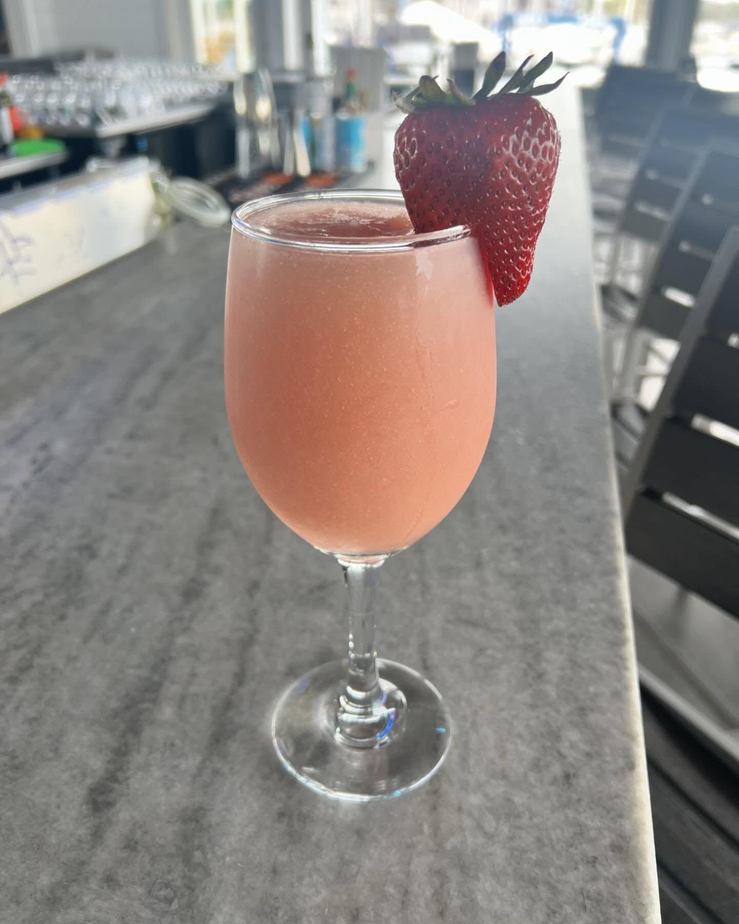 Pink cocktail in a stemmed glass, garnished with a strawberry, on a bar.