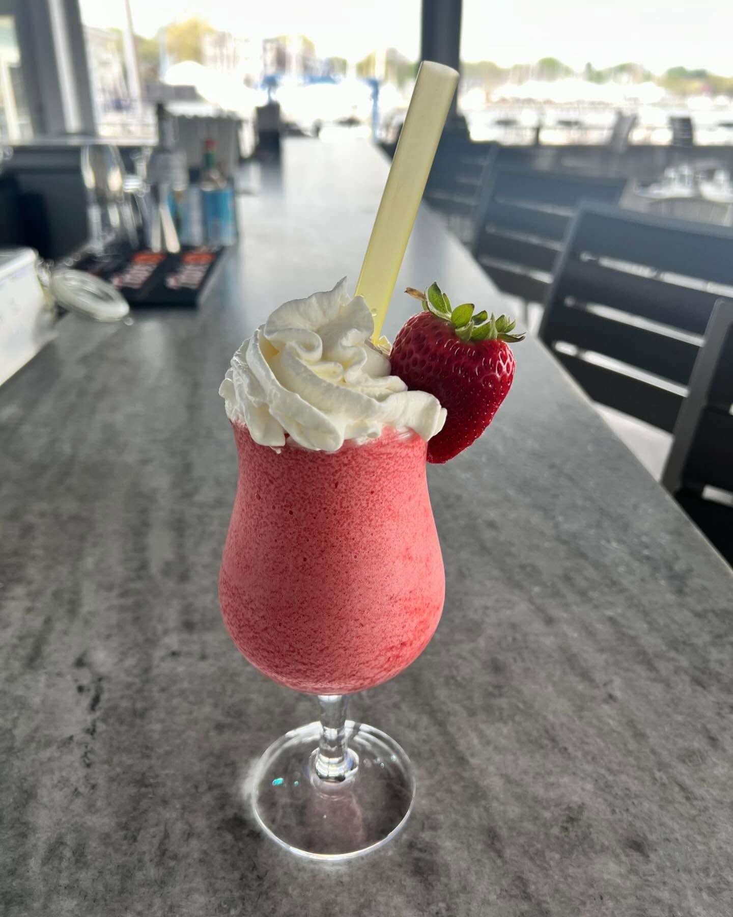 Strawberry smoothie in a glass with whipped cream and a strawberry garnish.