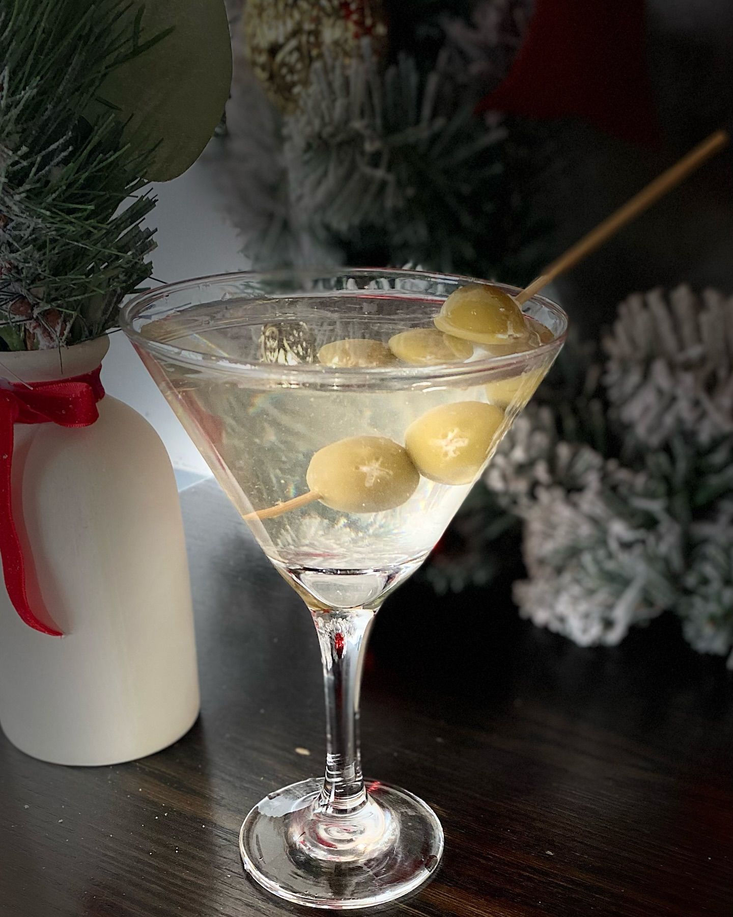 Martini cocktail with olives on a stick in a glass, next to a festive Christmas arrangement.