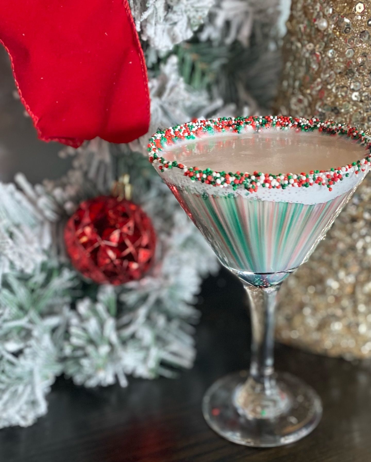 Christmas cocktail in a decorated glass with red, green sprinkles, near ornaments and greenery.