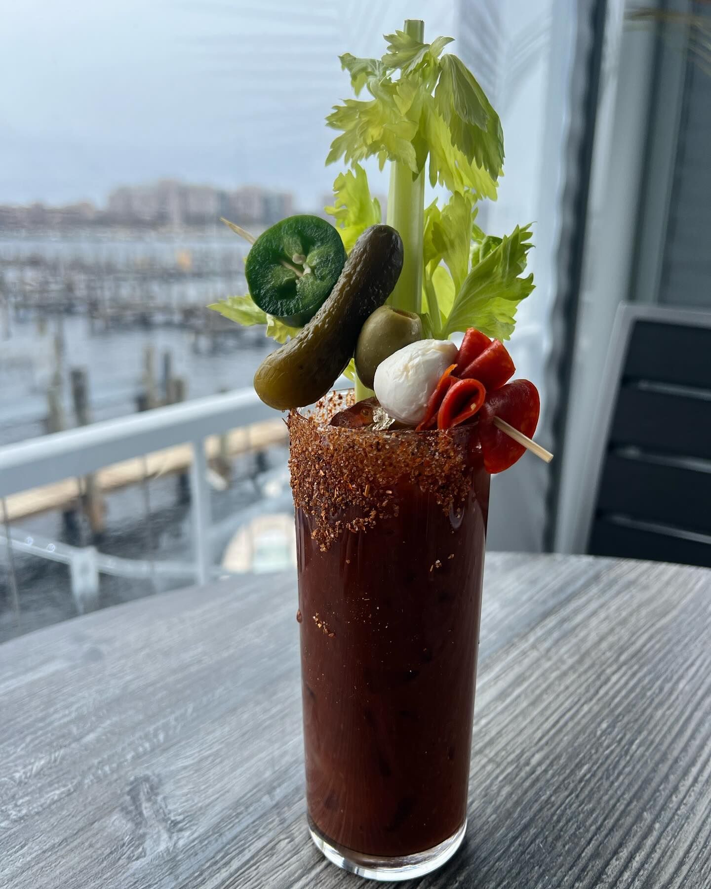 Tall Bloody Mary cocktail garnished with pickle, olives, jalapeno, celery, and red peppers.